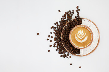 a cappuccino coffee cup with roasted brown beans is scattered on a white table with plenty of room for text. Composition Of a flat layer. Close-up, top view, white background.