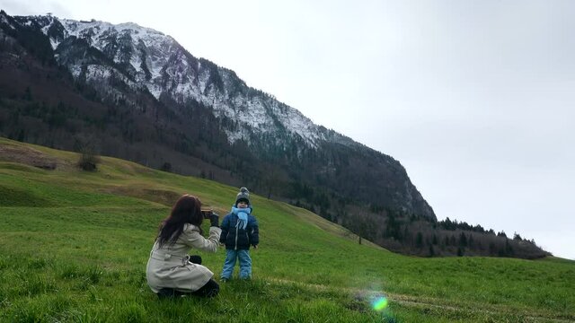 Mother Takes Pictures Photo on Smartphone of Little Child on Grass near Scenic Mountain Peak Stanserhorn. Ennetmoos Switzerland Europe
