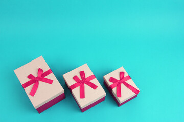three purple closed gift box different sizes with pink ribbon bow on turquoise background, top view with copy space