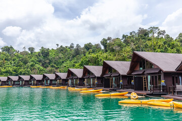 Fototapeta na wymiar Luxury Resort with Floating Raft Houses with Kayaks on Green Lake with Tropical Trees. Traditional Thai Bungalows at Cheow Lan Lake, Ratchaprapha Dam, Khao Sok National Park in Thailand, Surat Thani