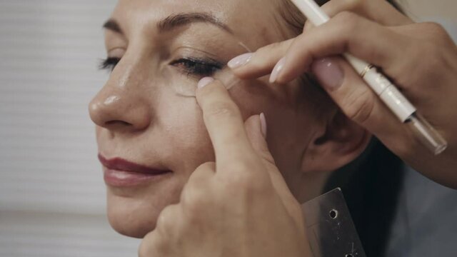 Closeup portrait of woman face with cosmetologist drawing correction lines as part of preparation for beauty procedure. Specialist marking points before operation.