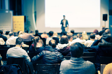 Speaker giving a talk in conference hall at business event. Rear view of unrecognizable people in audience at the conference hall. Business and entrepreneurship concept.