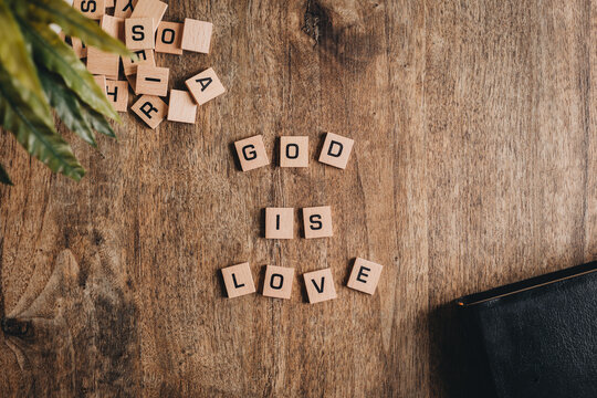 God is love spelled in block letters on a wooden table with a bible and a plant.