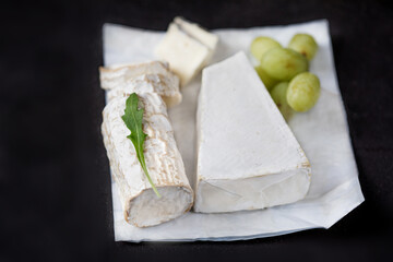 White goat cheese wih green grape on a  black background. Fresh goat cheese with copy space, cut in pieces