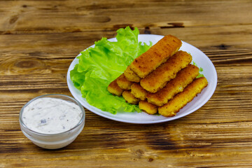 Fried fish fingers on a plate with lettuce and tartar sauce on wooden table