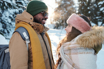 Amorous young intercultural dates in winterwear looking at one another
