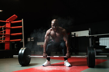 Fototapeta na wymiar African American heavyweight man doing barbell squats. The powerlifting coach screams and lifts the barbell in the smoke. Smoke from talcum powder in the gym