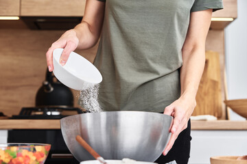 Woman in kitchen cooking a dough. Hands pour flour into a bowl