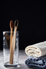 Fototapeta na wymiar Bamboo toothbrushes in glass and bathroom towels on dark background