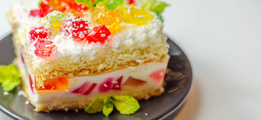 A portion of cream cake with pieces of colorful jelly and sprinkled with coconut flakes