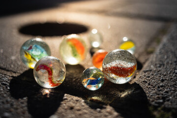 A group of marbles on the sidewalk near a marble pot illuminated by golden sun rays.