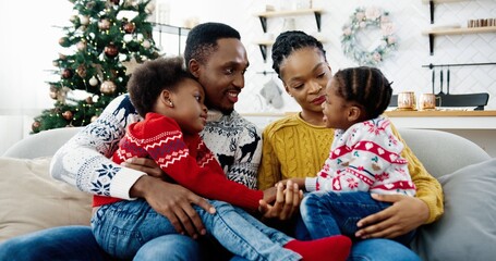 Close up of lovely African American family gathering together in decorated room at home on Christmas. Parents speaking and spending time with kids. Holidays concept. New Year mood