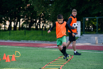 Obraz premium Motivated teen soccer players perform run exercises with overcoming obstacles applying racks on artificial soccer field.