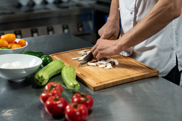 Hands of young male chef of modern restaurant cutting mushrooms on wooden board