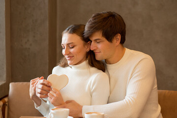 Young couple sitting in caffe with coffee and wooden heart. Valentine day.