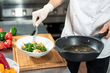 Gloved hand of young chef with fork and frying pan serving cooked meal