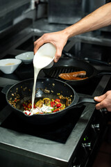 Hand of male chef pouring fresh milk into frying pan with vegetable stew
