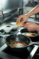 Hands of young professional chef grating cheese into frying pan with stew