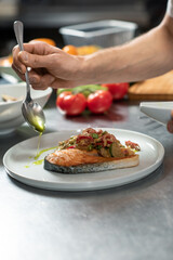 Hand of male chef adding olive oil to appetizing vegetable stew with salmon