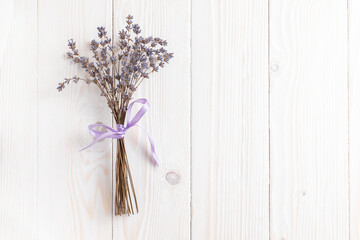 Bunch of dried lavender tied with purple ribbon on white wooden table.