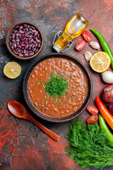 Vertical view of tomato soup oil bottle beans lemon and a bunch of green on mixed color table