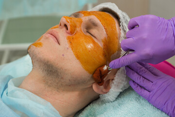 A nurse wearing gloves treats the skin of a male patient before undergoing cosmetic surgery