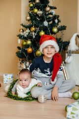 A little boy and his brother play with gifts under a festive Christmas tree. Happy Christmas and New Year celebrations