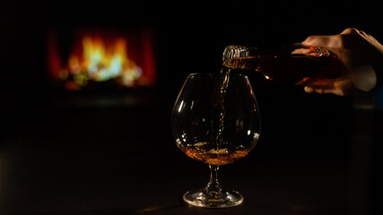 Close-up of a female hand with a glass of brandy on the background of the fireplace