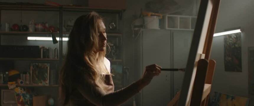 Female artist working on new painting inside her garage studio workshop. Shot with 2x anamorphic lens