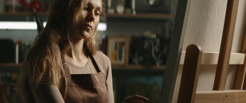 CU Portrait of female artist working on new painting inside her garage studio workshop. Shot with 2x anamorphic lens