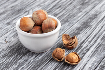 Whole hazelnuts in white bowl on black wooden table.