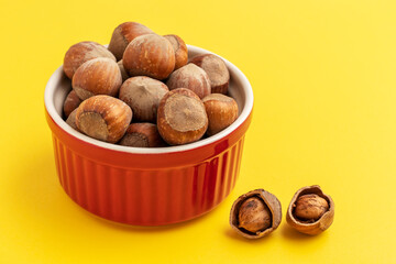 Whole hazelnuts in a red bowl on yellow background.