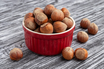 Whole hazelnuts in a red bowl on a black wooden table.