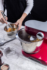 mixer working and behind woman beating eggs with her hands. Concept of cooking and pastry at home, blog, classes, social networks and small businesses. Vertical photo and selective focus.
