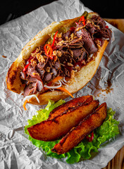 Philly cheese steak sandwich with meat, vegetables, cheese and sause on wooden table. street food