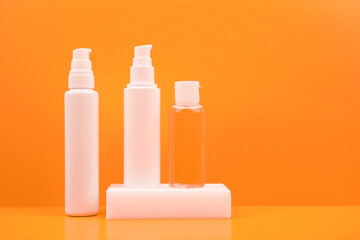 Set of three cosmetic products, face cream, cleaning foam and lotion in a transparent bottle against bright orange background. The concept of daily skin care or anti aging products with fruit extracts