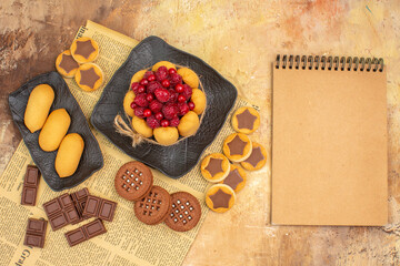 Tasty cake different biscuits on brown plate and notebook on mixed color background