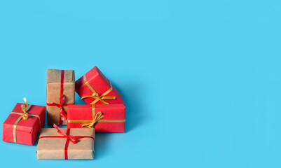 A lot of boxes with gifts in red and natural paper with gold and red ribbons on light blue background. Copy space. Banner