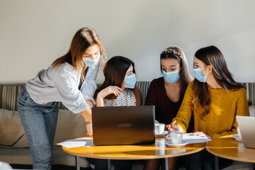 A group of girls in masks sit in a cafe and work on laptops. Teaching students.