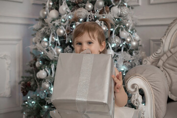 a girl in a beige dress stands in the room next to the christmas tree and holds a gift