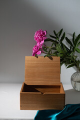 Large wooden box with a separator on a light mint background empty. Product Display Concept. Large pink peonies in a transparent vase. Copy space. Oak box on the table, for installation