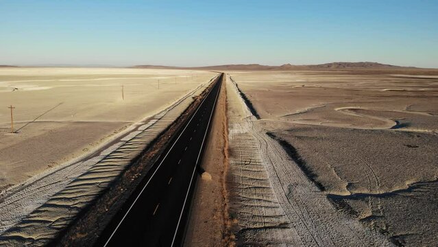 Drone flying over blacktop road in the desert bare except power lines and rocks salt flats