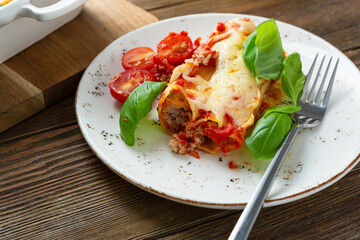 Baked canneloni on white plate on wooden table