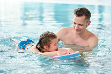 Happy young father teaching his little daughter to swim in pool in spa center