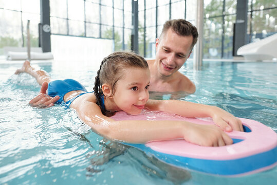 Happy young active man teaching his little daughter to swim at leisure center