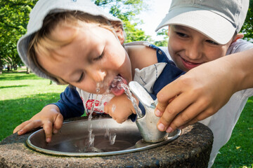 Little boy drinking tab water with the help of his brother