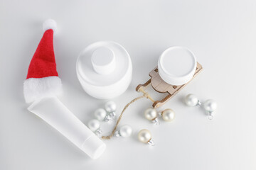 Obraz na płótnie Canvas New Year's cosmetic concept. Top view of white jars of cream and tubes on white tables and wooden sledges with santa hat. Copy space