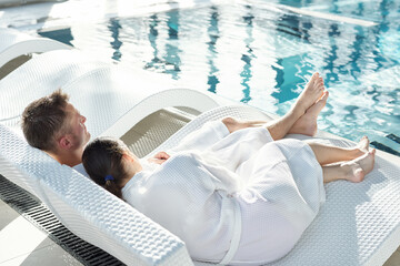 Tired young brunette woman in white bathrobe keeping head on husband shoulder