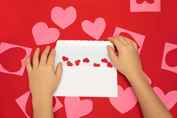 Valentine's day message in white envelope on red background. Human hands fold hearts valentines