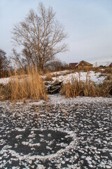 Frosty evening on the lake. Transparent ice with snowflakes in the form of stars. Dry, frozen grass. Village on the shore.